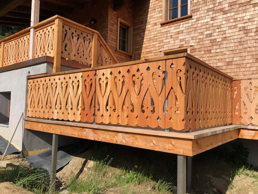 Balkon mit ornamentalem Holzgeländer an Schindelfassade